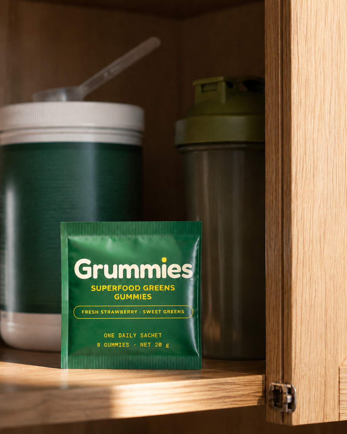 A tub of greens powder pushed to the back of a kitchen cupboard with one sachet on the bench